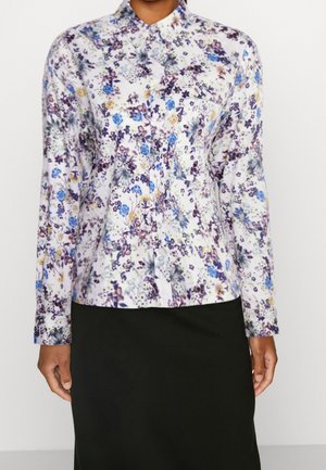 Blusa blanca de manga larga con estampado floral multicolor, con botones en la parte delantera, usada con una falda negra por una persona de pie.