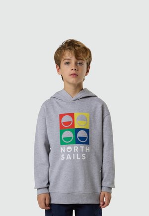 Niño con cabello rizado castaño claro que lleva una sudadera con capucha gris con logotipos cuadrados en rojo, amarillo, verde y azul, y texto "NORTH SAILS" en el frente.