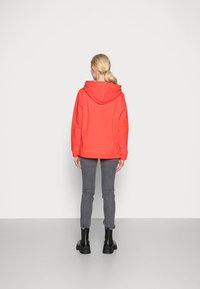 Rode hoodie met een ontspannen pasvorm, in een effen kleur, en geribbelde manchetten, gecombineerd met grijze skinny jeans en zwarte enkellaarsjes.