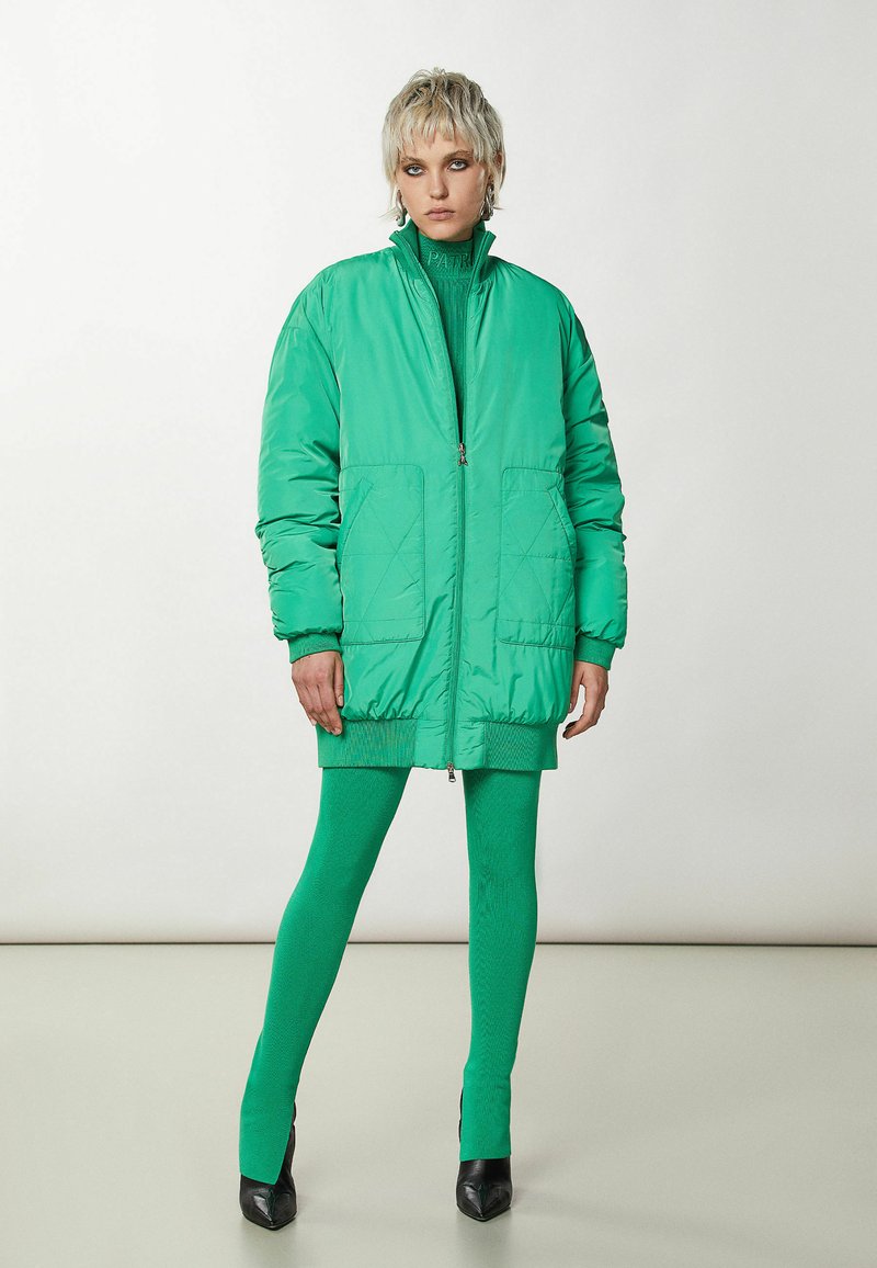Jasnozielona kurtka z ociepleniem, zapinana na zamek, z dwoma przednimi kieszeniami, żebrowanym dołem i długimi rękawami, połączona z pasującymi zielonymi legginsami i obcasami.