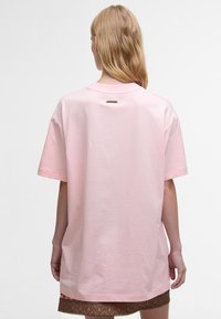 Ροζ βαμβακερό t-shirt με κοντά μανίκια, χαλαρή εφαρμογή, επιμηκυμένο πίσω μέρος και μια μικρή χρυσή λεπτομέρεια στον λαιμό. Λαμπερή υφή.