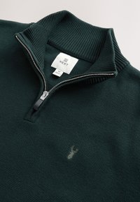 Pull côtelé vert foncé à fermeture éclair quart de zip argentée, petit logo cerf brodé sur la poitrine et étiquette de marque blanche NEXT à l'intérieur du col.