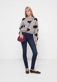 Sivi pulover s maroon uzorcima srca, tamnoplave uske traperice i maroon lakirane cipele. Mala burgundska torba preko ramena.