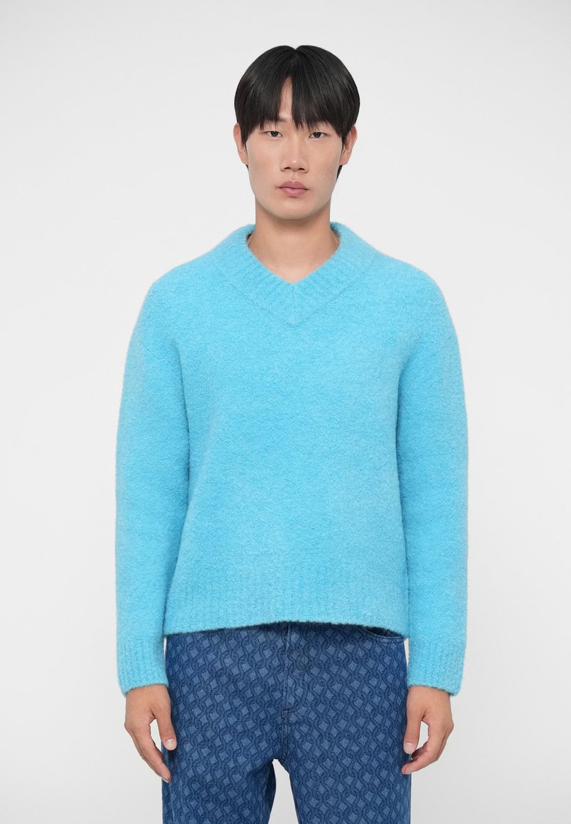 Lichtblauwe v-hals trui met een zachte textuur en een relaxed fit, voorzien van geribbelde manchetten en een iets langere achterzoom. Gecombineerd met gestreepte denim.