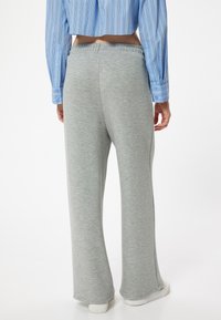 Graue Sweatpants aus weichem Material, mit einem lockeren, ausgestellten Design und einem elastischen Bund. Tragen Sie dazu ein blau gestreiftes Crop-Top.