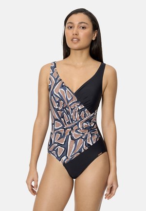 Mujer con un traje de baño de una pieza sin mangas, con patrones geométricos abstractos en negro, marrón, azul y beige, de pie frente a un fondo liso.