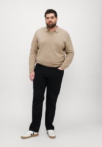 Beige langermet polo-skjorte med krage, kombinert med svarte jeans og hvite sneakers. Teksturen er glatt, med en avslappet passform.