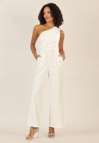 Weiße ein-schulter Jumpsuit mit drapiertem Oberteil, weitem Bein und seitlichen Taschen. Glatter Stoff mit minimalistischen Design. Silber-akzentuierte Absatzschuhe.