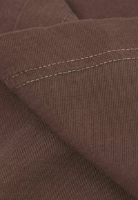 Hnědá žebrovaná látka s texturovaným povrchem a viditelným prošíváním podél okrajů, která vykazuje hloubku díky překrývajícím se vrstvám.