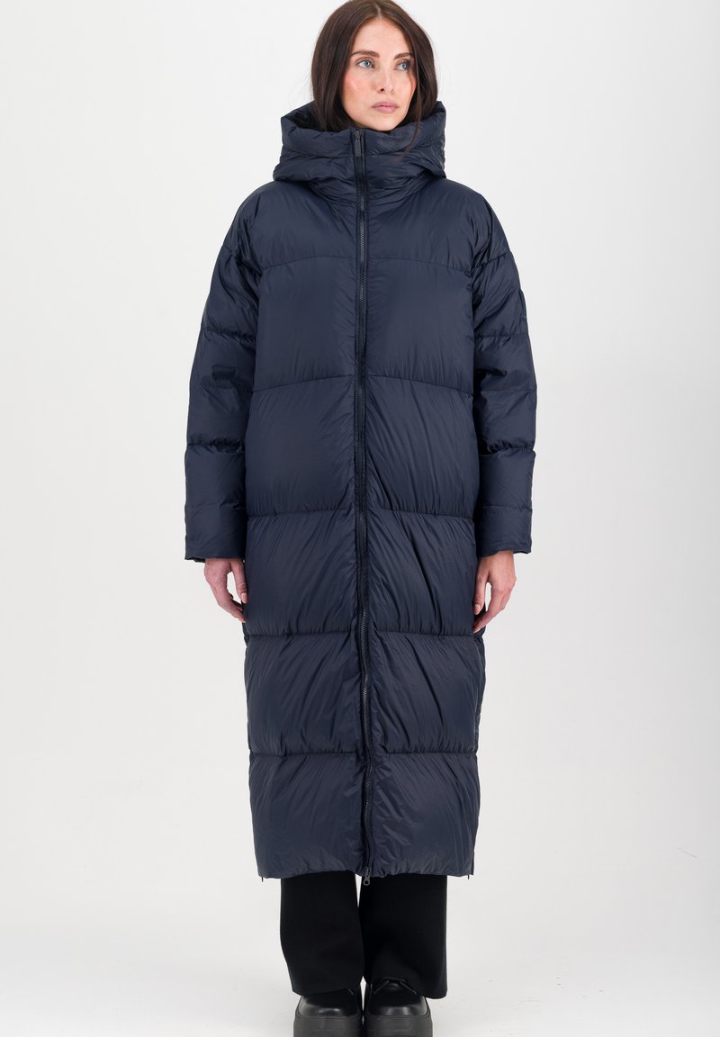 Donkerblauwe gewatteerde jas met capuchon, met een lange uitstraling, gestikte gedeelten en een rits aan de voorkant. Glad textuur met een lichte uitstraling.