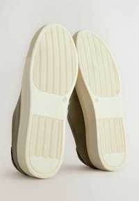 Chaussures grises avec une texture lisse et des semelles en caoutchouc blanches. Les semelles comportent un motif de bande de roulement ondulé pour une meilleure adhérence. Vue du dessous.