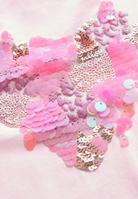Nahaufnahme eines pinkfarbenen Stoffes, der mit glänzenden Pailletten und Glitzer verziert ist und ein strukturiertes und farbenfrohes abstraktes Muster schafft.