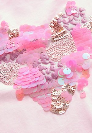Nahaufnahme eines pinkfarbenen Stoffes, der mit glänzenden Pailletten und Glitzer verziert ist und ein strukturiertes und farbenfrohes abstraktes Muster schafft.