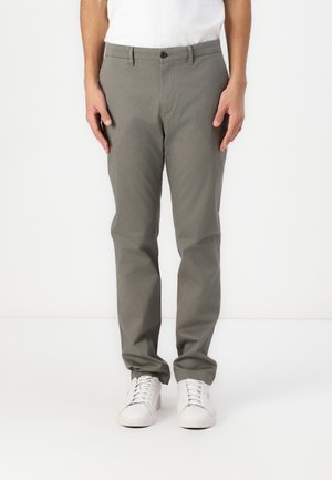 Slim-Fit, hellgraue Hose aus Baumwoll-Mischgewebe. Mit Knopfverschluss, Gürtelschlaufen und Seitentaschen. Getragen mit weißen Sneakers.