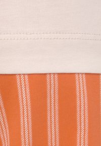 Tejido de punto a rayas en naranja y blanco, con una sección superior lisa en color beige claro. Detalle de costura visible en la unión entre las telas.