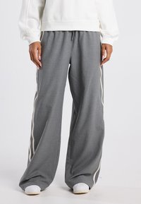 Grijze wijde broek van een textuurstof, met een crèmekleurige zijkantstreep en een tailleband met trekkoord, gecombineerd met witte sneakers.