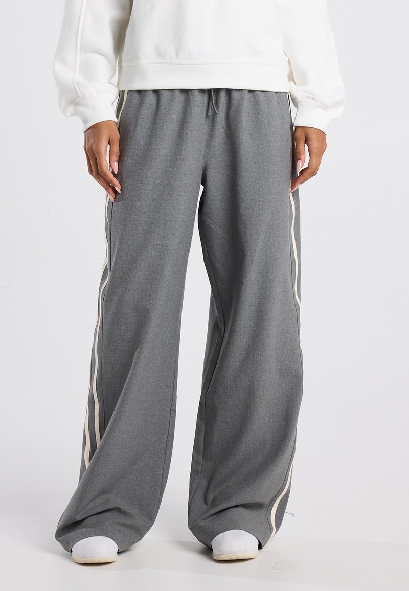 Grijze wijde broek van een textuurstof, met een crèmekleurige zijkantstreep en een tailleband met trekkoord, gecombineerd met witte sneakers.