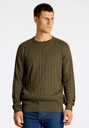 Maglione a trama a coste verde oliva con motivi a treccia, scollatura rotonda e maniche lunghe, abbinato a jeans blu.