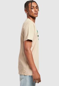 Beige bomulds-t-shirt med korte ærmer, med et grafisk design på forsiden. Lys blå denimjeans med en afslappet pasform.