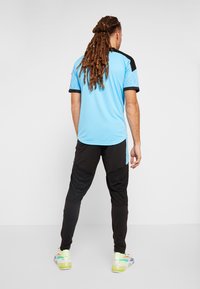 Hellblaues Sportshirt mit schwarzen Akzenten und kurzen Ärmeln, kombiniert mit schwarzen Hosen mit strukturierten Einsätzen und bunten Turnschuhen.
