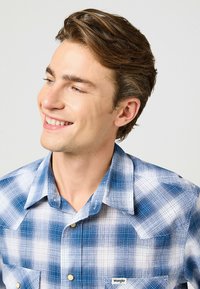 Sininen ja valkoinen ruutupaita kevyestä kankaasta, jossa on nappikaulus, kaksi etutaskua ja hienovaraisia tekstuurityksiä.