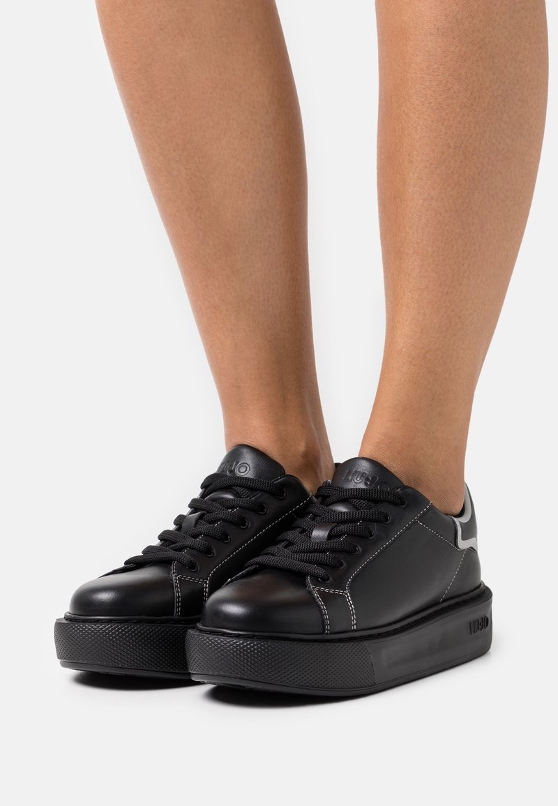 Svarta lädersneakers med tjocka gummisulor, runda tår, snörningsdesign och kontrasterande sömdetaljer.