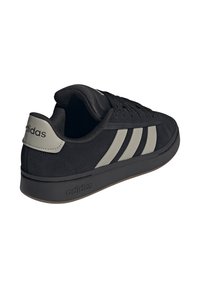 Schwarzer Adidas Sneaker mit grauen Streifen und Fersenschlaufe, Schnürdesign und Gummisohle, schräg gehalten, um die Rück- und Seitenansicht zu zeigen.