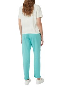 Korte mouwen, crèmekleurig en wit gestreept shirt gecombineerd met licht turquoise broek. Witte sneakers maken de outfit compleet.