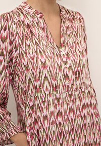 Multicolored blouse featuring a pink, green, and brown abstract pattern, with a collared neckline, button front, and gathered long sleeves.