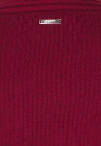 Burgundyrandig stickad tyg med liten rektangulär silvermetall Esprit-märkesetikett sydd nära den övre mitten.