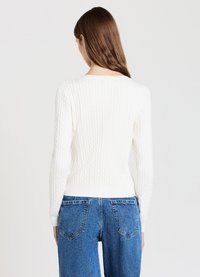 Weißer Strickpullover mit langen Ärmeln und einem weiten Rundhalsausschnitt, ausgestattet mit gerippten Bündchen und Saum. Kombiniert mit hochgeschnittenen blauen Jeans.