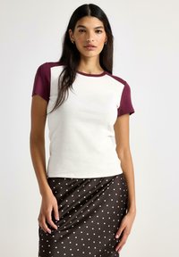 T-shirt med korta ärmar i krämfärgad kropp och burgundiska raglanärmar, med rund halsringning och mjuk bomullstextur.