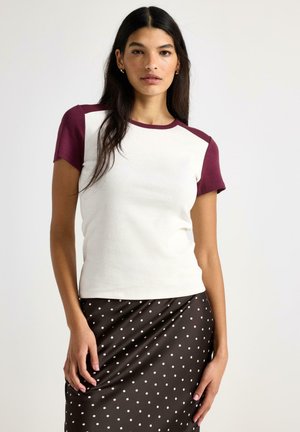T-shirt med korta ärmar i krämfärgad kropp och burgundiska raglanärmar, med rund halsringning och mjuk bomullstextur.