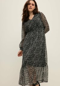 Vestido negro con mangas largas transparentes, escote en V y un estampado de leopardo gris por toda la prenda. Presenta una cintura ajustada y una falda fluida con volantes.