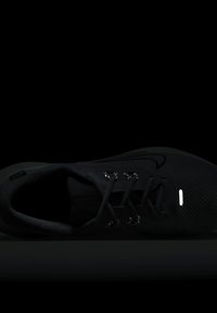 Chaussure de sport noire avec une tige en maille, accents réfléchissants et lacets plats. Comprend un col rembourré et une semelle texturée pour une meilleure adhérence.