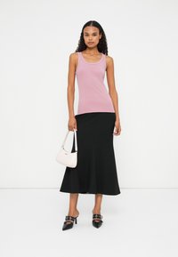 Lichtroze tanktop met een ronde hals, gecombineerd met een zwarte midi-rok. Accessoires zijn een kleine roze handtas en zwarte hakken.