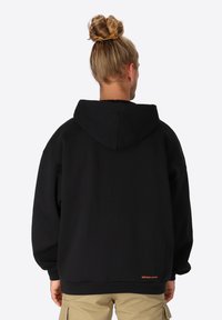 Zwarte hoodie met een relaxed fit, voorzien van een trekkoord capuchon, lange mouwen en een klein oranje logo op de onderrug. Gemaakt van een katoenmix.