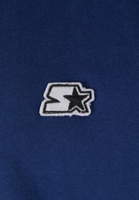 Kék szövet, texturált felülettel, fehér hímzett logóval, amely egy fekete körvonalú 'S' betűből és egy csillagból áll.