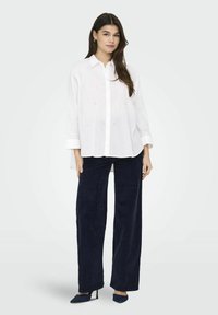 Valge nööpidega shirt, millel on südame muster, koos tumesiniste laiadest lõikepükstega ja siniste teravate kontsadega. Silene tekstuur, mugav lõiked.