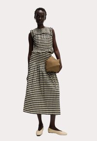 Svartvit rutigt mönstrad topp och kjol med veck. Ljusbrun texturerad väska med mjuka kanter. Modell i cremefärgade ballerinaskor. Minimalistisk stil.
