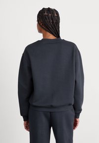 Sweatshirt à col rond de couleur gris foncé, à manches longues, avec des poignets et un ourlet côtelés. Le matériau semble doux avec une texture lisse. Aucun logo ni motif visible.