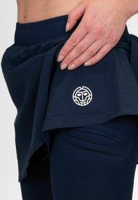 Falda deportiva azul marino con cintura elástica, que presenta un logotipo distintivo y un diseño en capas. La tela parece ligera con una textura suave.