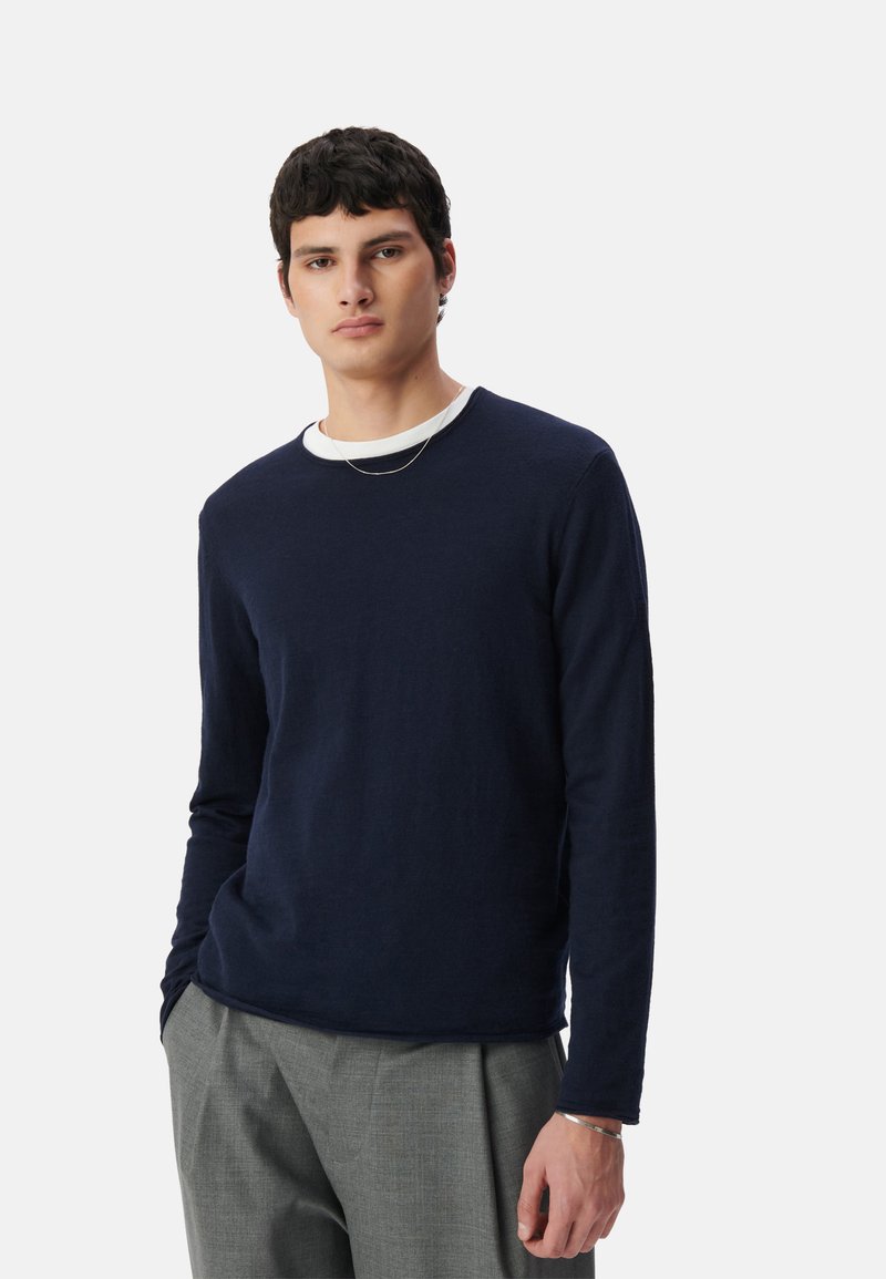 Granatowa koszula z długim rękawem, uszyta z miękkiego, strukturalnego materiału, z okrągłym dekoltem i białym wewnętrznym kołnierzykiem, zestawiona z szarymi, dopasowanymi spodniami.