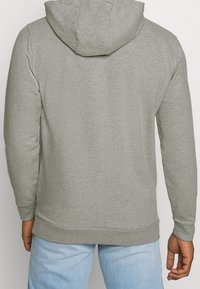 Sudadera gris de textura suave, con capucha, mangas largas y dobladillo recto. Combinada con pantalones de mezclilla azul claro.