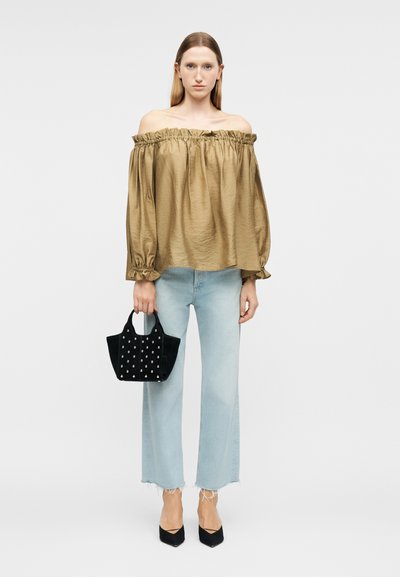 Γυναίκα που φοράει ένα χρυσό τοπ με ακάλυπτους τους ώμους, ανοιχτό μπλε τζιν παντελόνι μέχρι τον αστράγαλο, μαύρες αιχμηρές γόβες και κρατά μια μαύρη τσάντα με τρουκς.