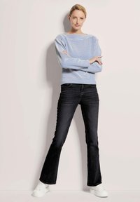 Helles blaues und weiß gestreiftes Langarmoberteil, dunkle Schlagjeans und weiße Sneaker. Das Oberteil hat einen Bootsausschnitt und eine lockere Passform.