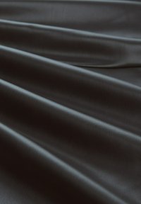 Schwarzer, strukturierter Stoff mit glatter Oberfläche, der weiche, fließende Falten und subtile Unterschiede in Licht und Schatten zeigt.