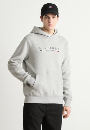 Sudadera de algodón gris con un bolsillo canguro en la parte frontal y puños acanalados. Presenta el logo "HILFIGER NEW YORK" con acentos rojos y azules. Gorra negra.