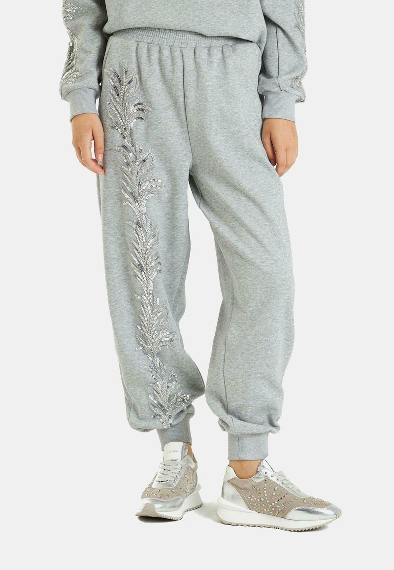 Graue Jogginghosen mit gestickten floralen Mustern aus silbernem Faden, mit gerippten Bündchen und einem elastischen Bund. Kombiniert mit stylischen Sneakers.