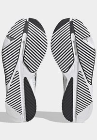 Buty sportowe z białą i czarną paskowaną gumową podeszwą, posiadające teksturowaną powierzchnię i smukły design z detalami wentylacyjnymi.